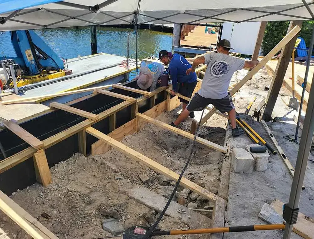 Crew working on modern seawall repair using wood formwork and reinforcement materials along the shoreline.